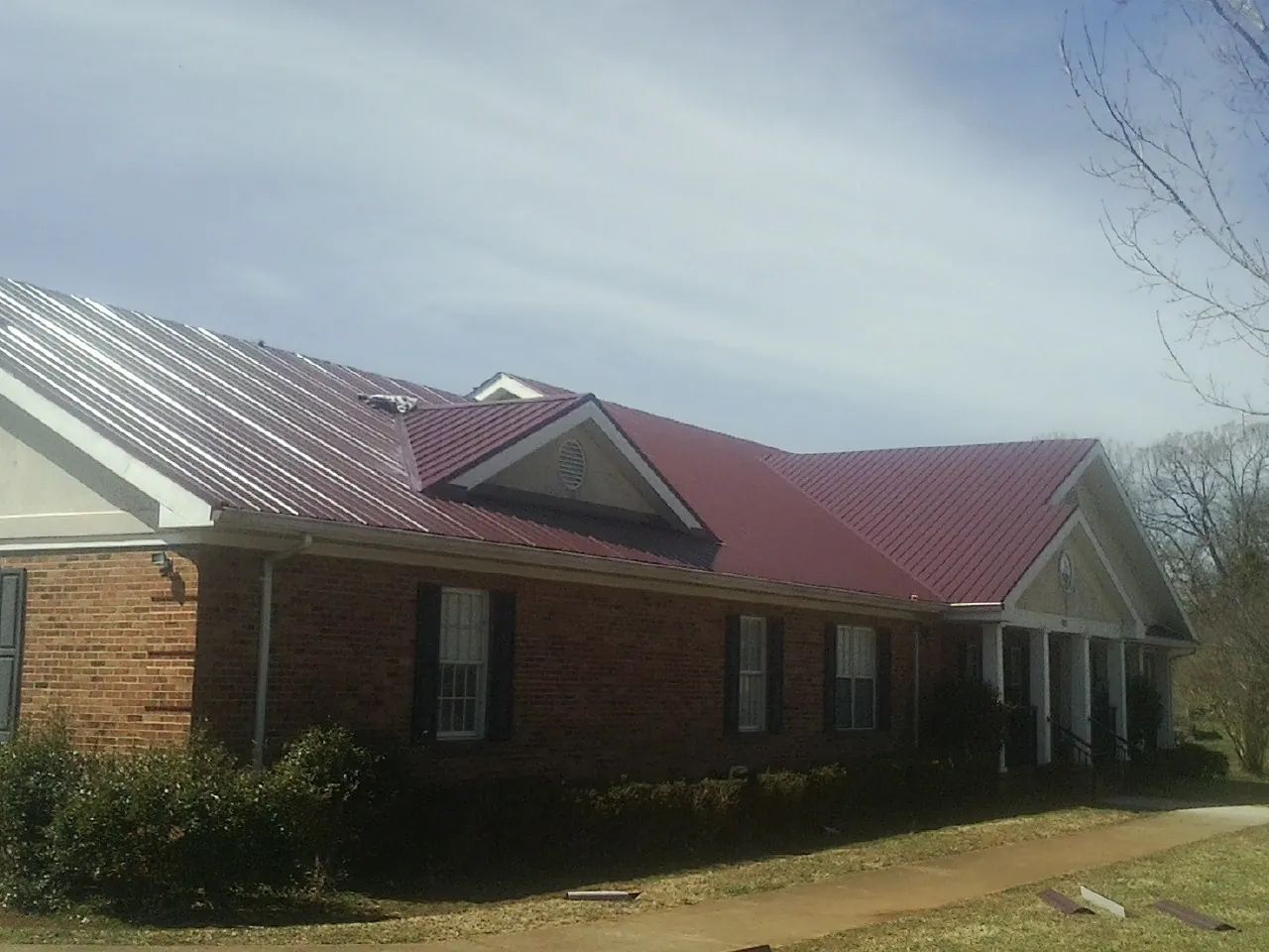 Red metal roof with gabled entries on a long brick building, from a Hail Damage Roof Repair job in Deepwater