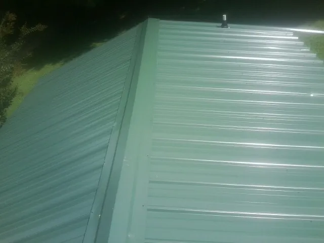 New green metal panels meeting at the ridge of a roof — Flat Roof Repair work by our crew in Deepwater